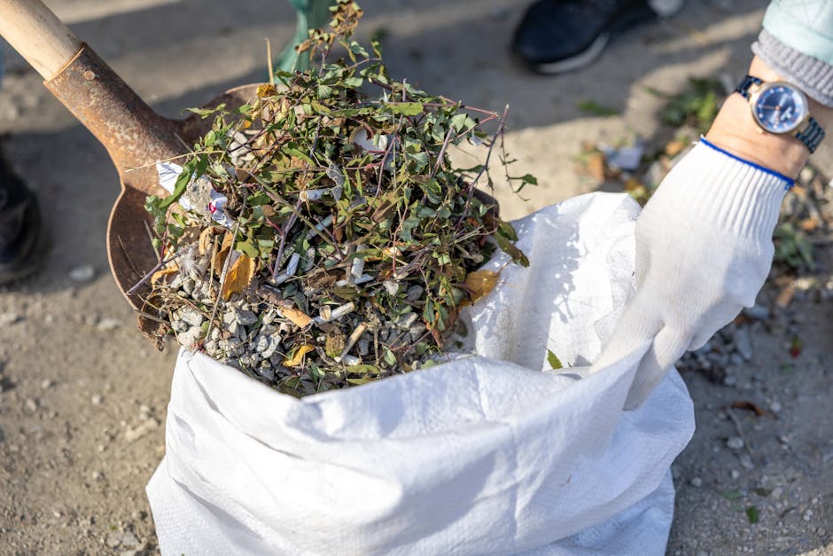 A pile of construction debris and discarded materials is spread across the ground in front of a partially damaged multi-storey apartment building. The debris includes broken bricks, concrete fragments